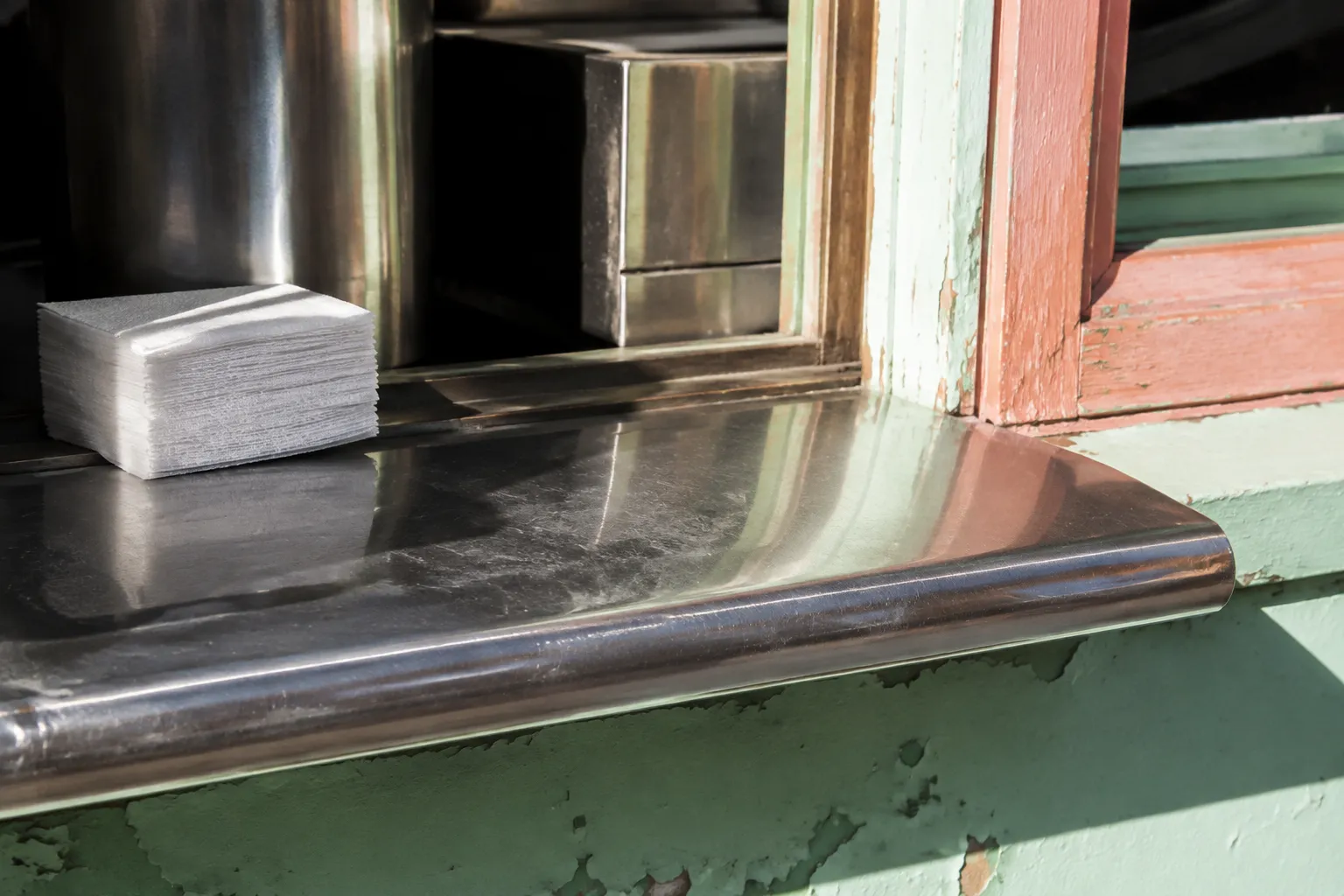 Close-up of a Cuban coffee ventanita counter with stainless steel and pastel window frame