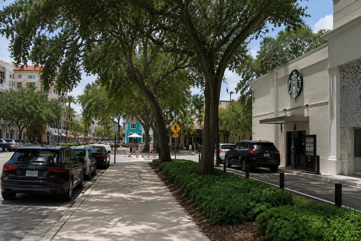 Grand Avenue in Coconut Grove showing Starbucks and storefronts with pedestrians and parked cars under oak trees