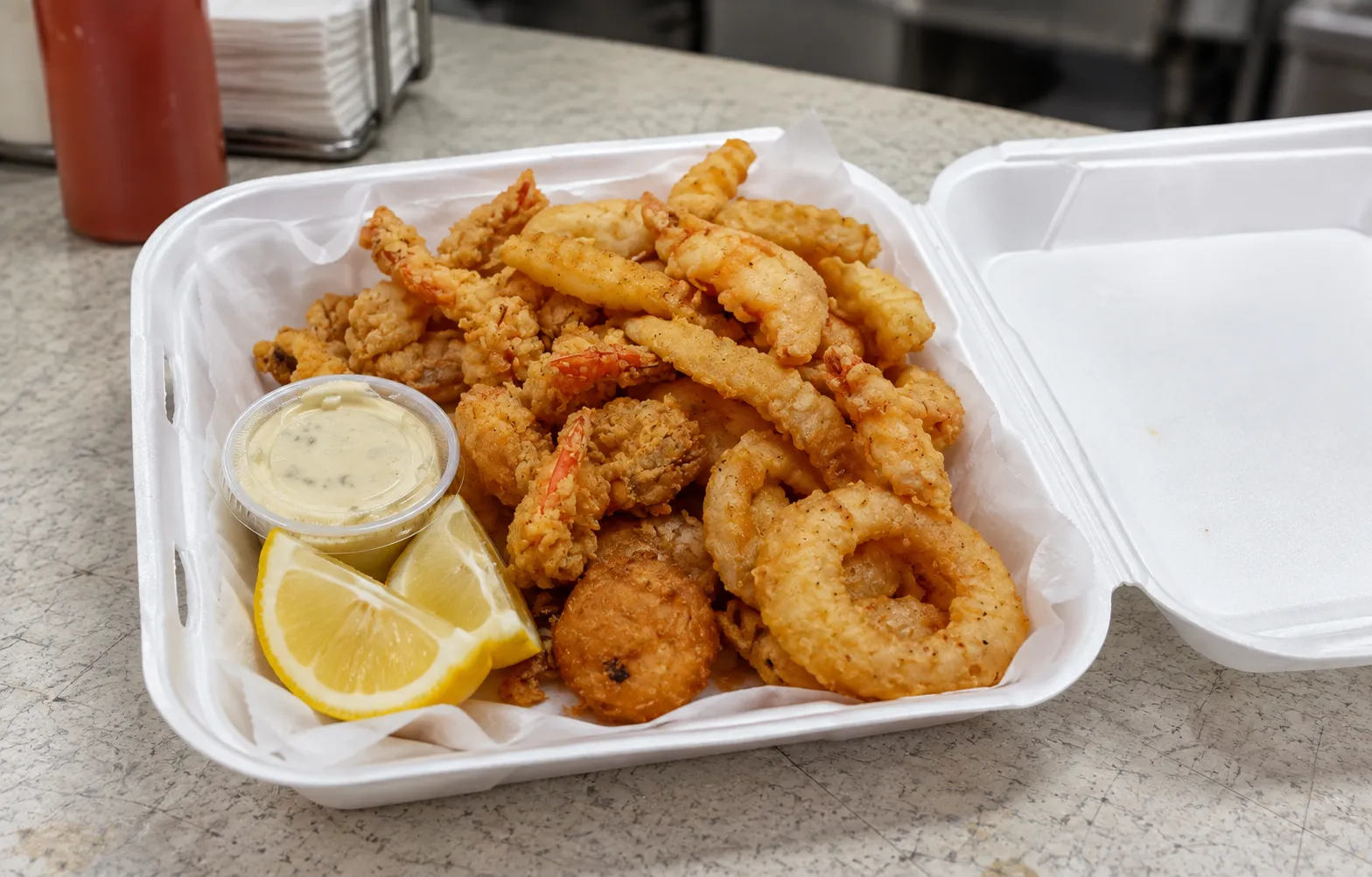 A paper tray of golden fried shrimp with lemon wedges and a small tub of sauce on a formica counter
