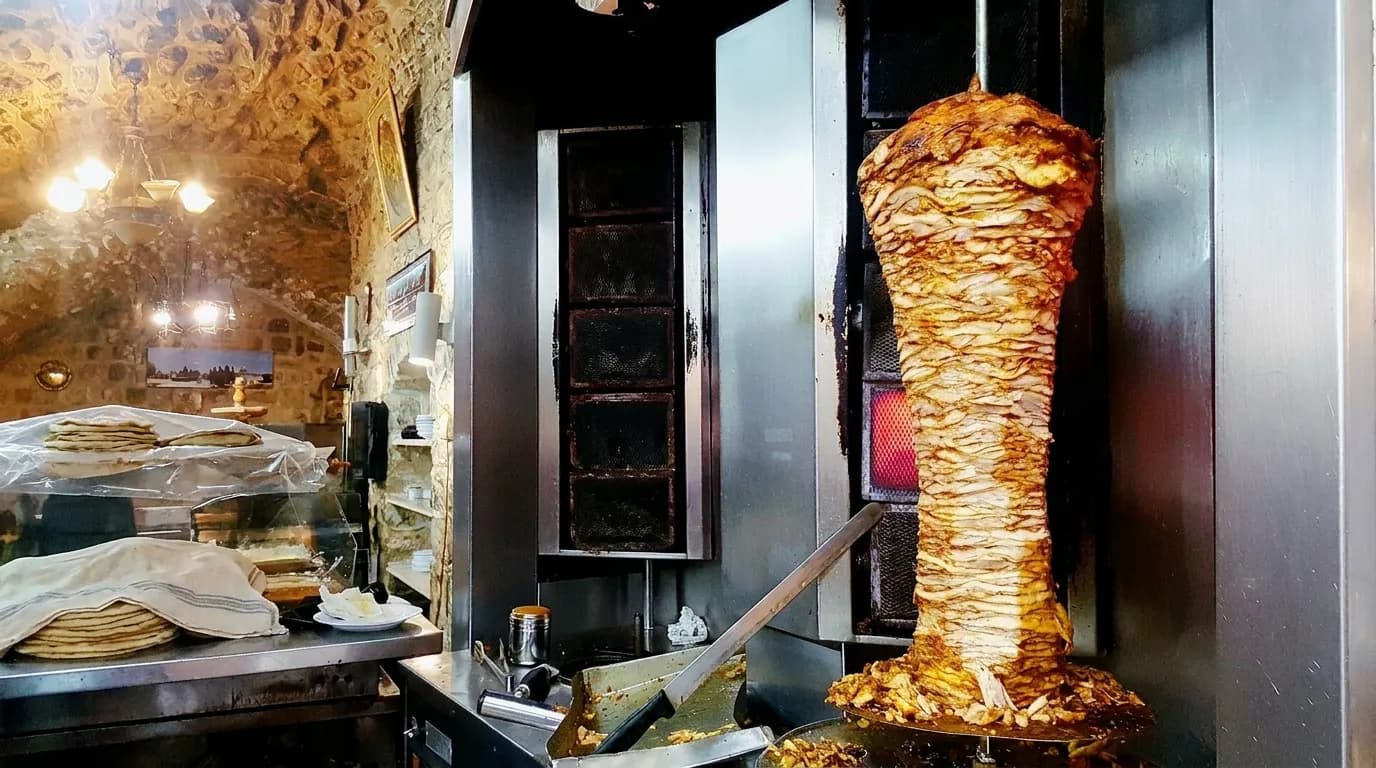 A vertical rotisserie of meat behind a counter with a carving knife resting on the guard