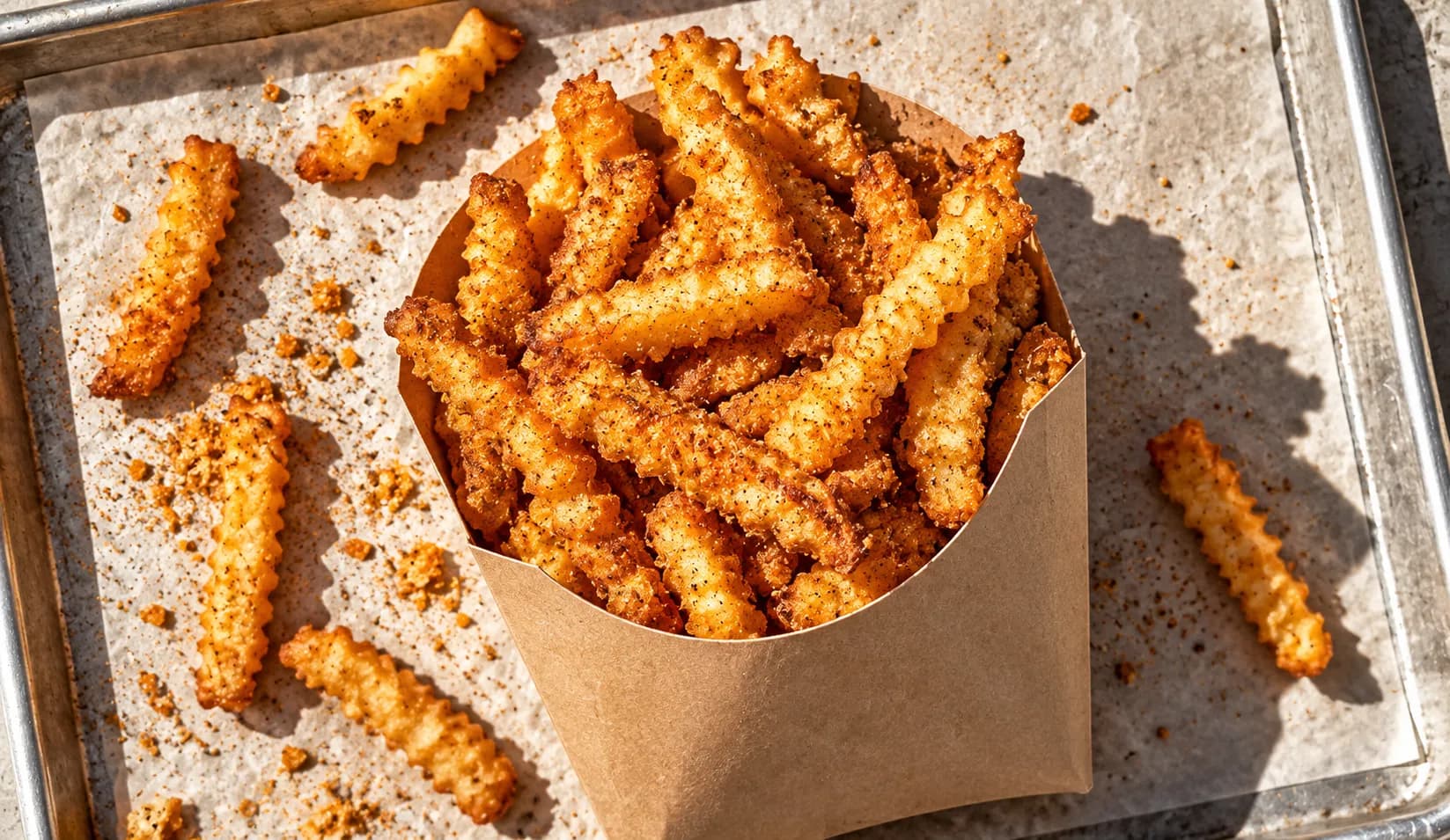 Heavily seasoned crinkle fries piled in a paper carton with visible spice coating and crisp edges on a tray