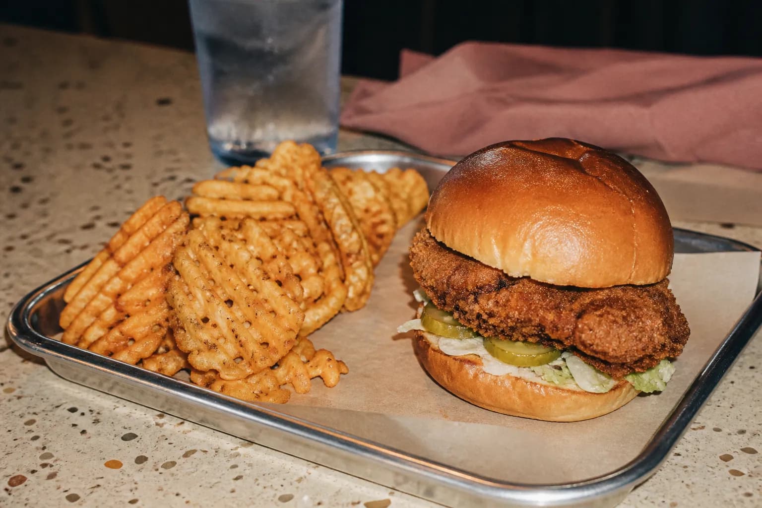 A breaded chicken sandwich and a carton of crispy waffle-cut fries served on a tray