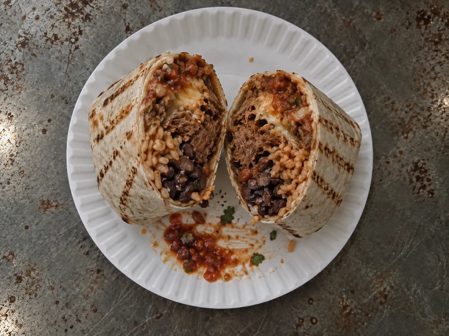 A cut burrito showing layered filling on a paper plate