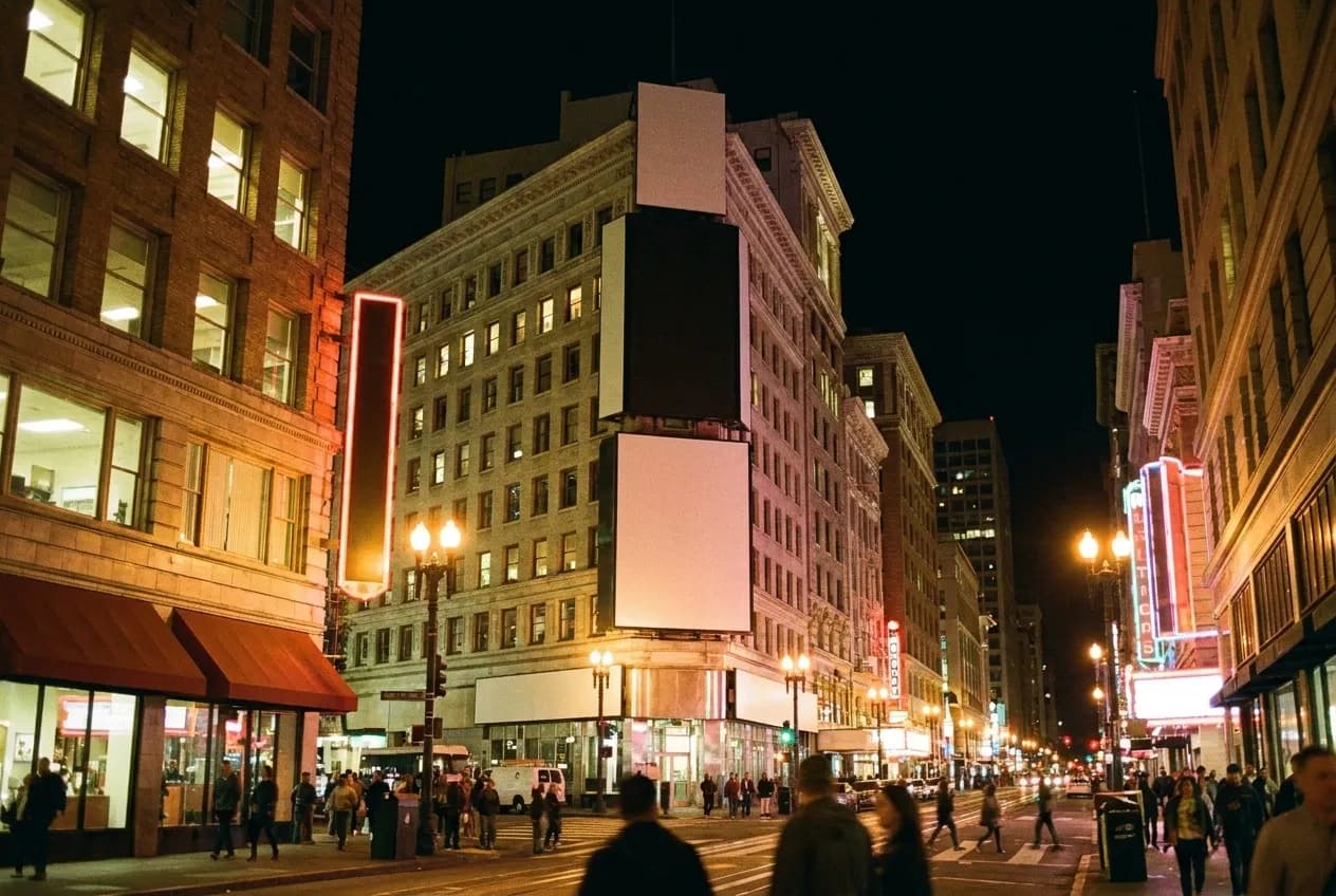 A neon-lit city corner at night with a crowd on the pavement and old commercial buildings above