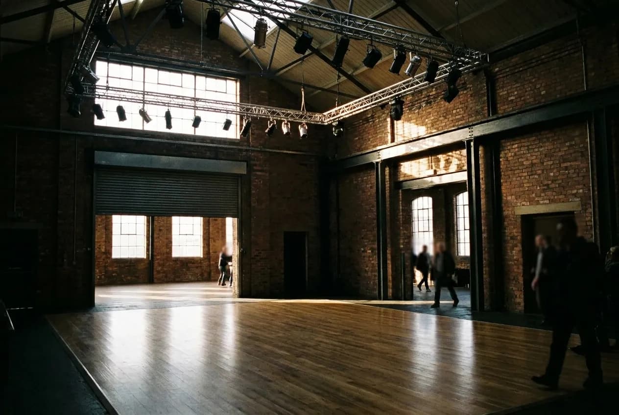 A dark warehouse-style room with a wooden dance floor and overhead lighting rigs