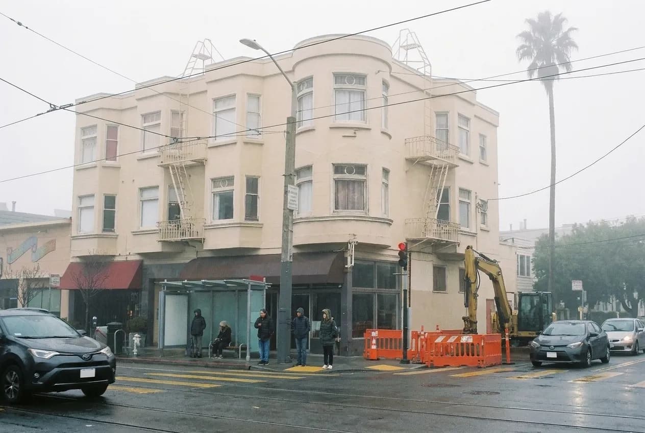 A foggy neighbourhood street corner in San Francisco with low shopfronts and a bus stop