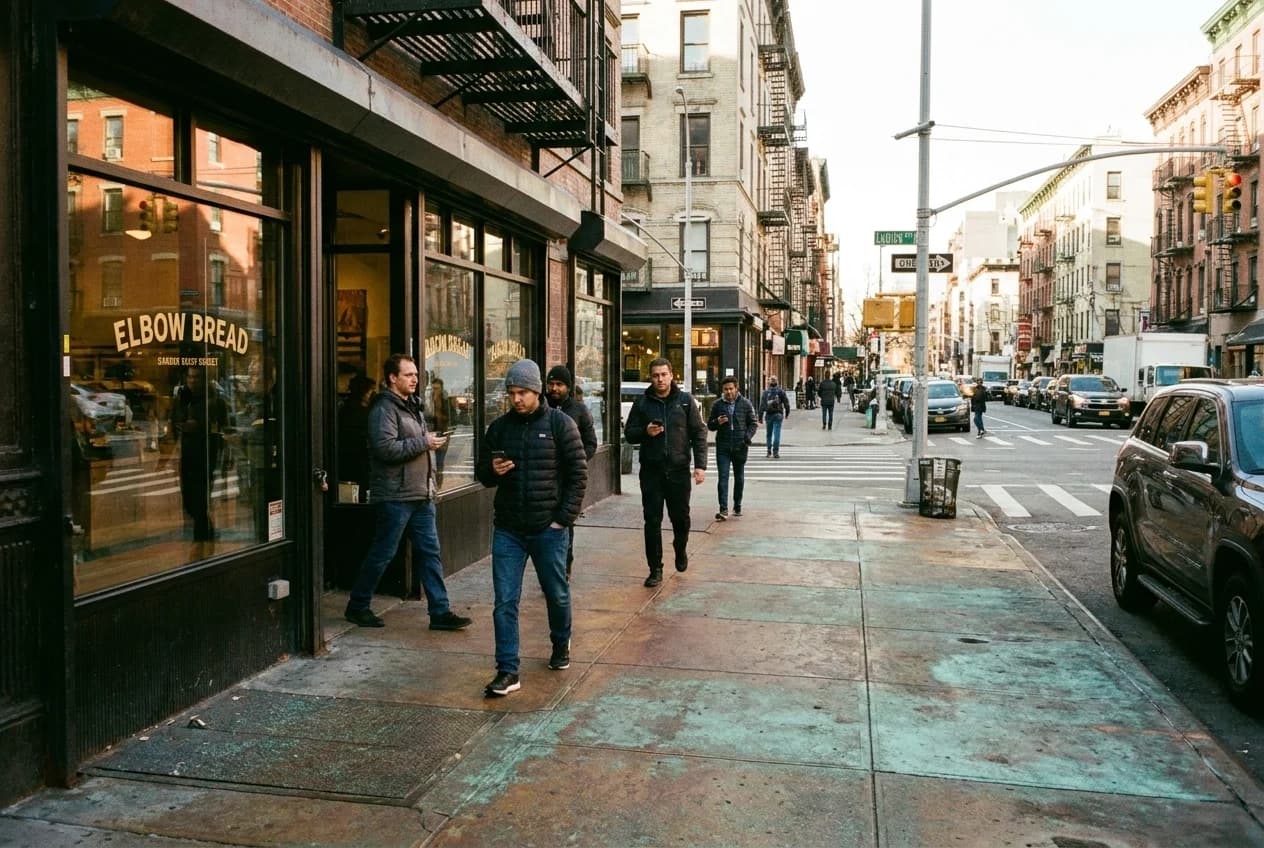 Corner of Ludlow and Division Streets with Elbow Bread storefront and morning pedestrians on the Lower East Side.