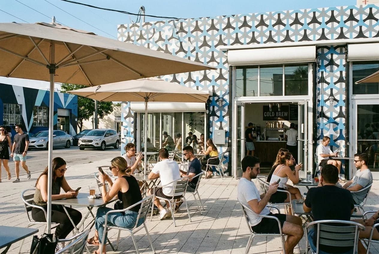 Outdoor café patio with shade umbrellas and mural-covered building façade in Wynwood, Miami