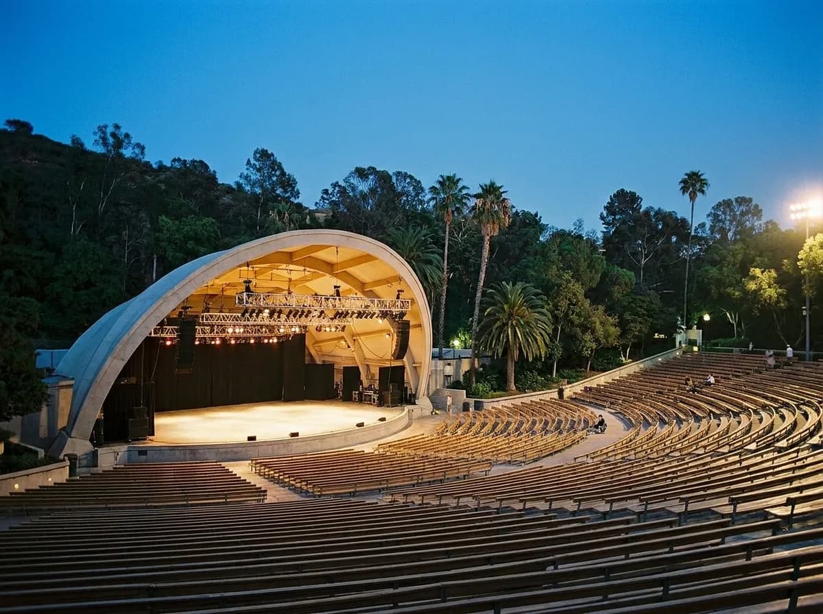 A large tiered outdoor amphitheatre at dusk with stage lighting rigs above a broad empty stage