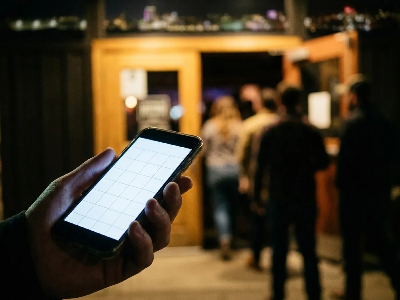 A hand holding a phone showing a blank calendar grid, with a lit venue entrance out of focus behind