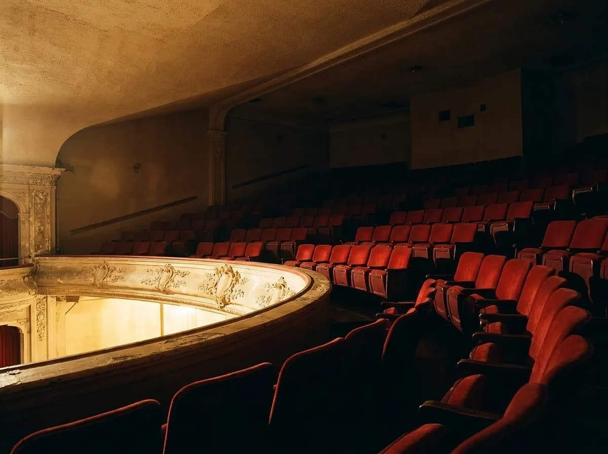 An ornate theatre balcony and stage lit in warm colour from below with empty seats