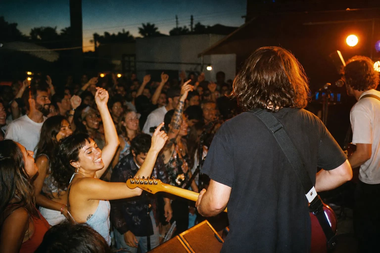 Warm-lit crowd with hands raised at an intimate live-music show at dusk