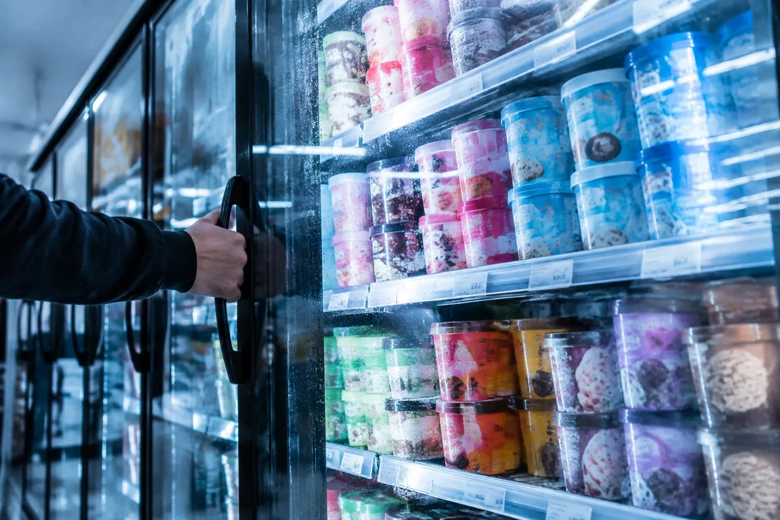 Close view of a grocery store freezer aisle with glass doors and stacked ice cream pints