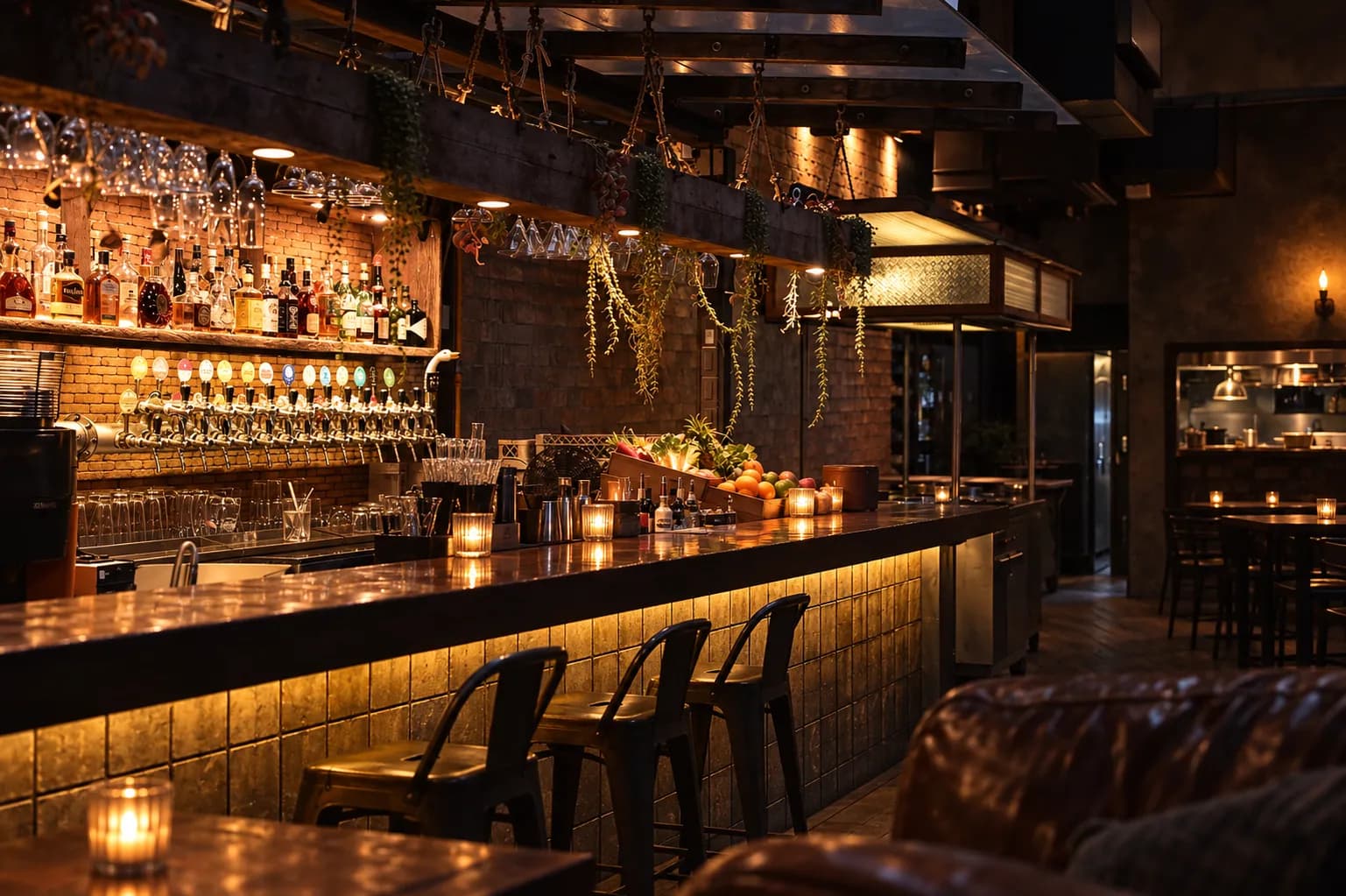 Small dim back-room bar with a wall of agave bottles on timber shelves, votive candles clustered along the bar top and a worn leather sofa in the foreground