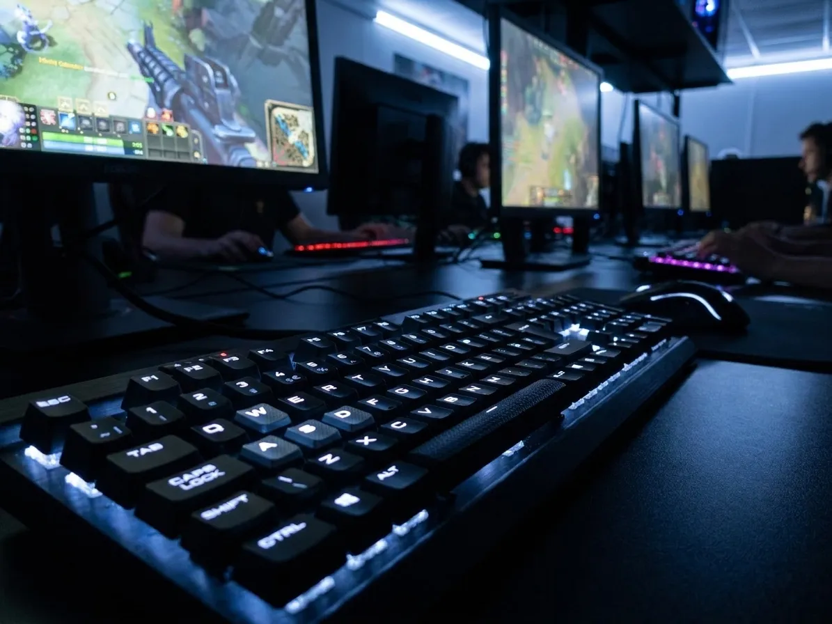 High-performance gaming PC with RGB mechanical keyboard, gaming mouse, and monitor displaying competitive game interface in a LAN center environment