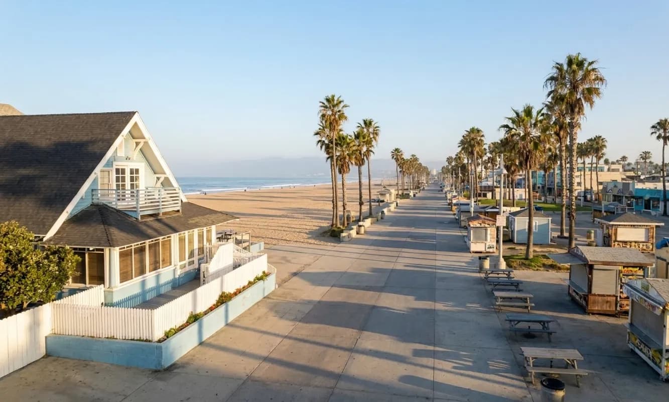 Venice Beach Boardwalk stretching north along Ocean Front Walk with vendor stalls, palm trees, and the Pacific Ocean visible to the west