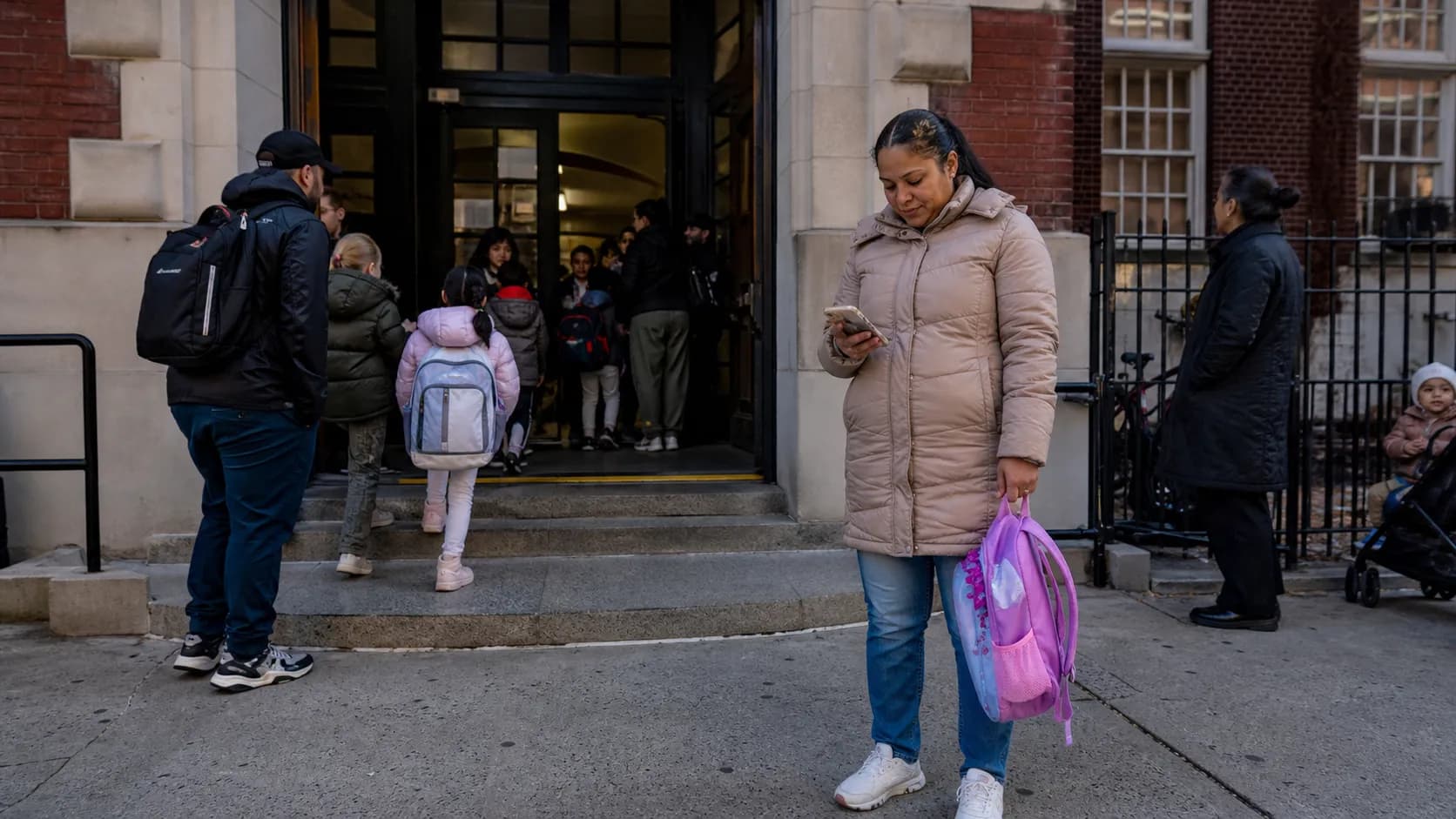 Parent and young child standing outside a New York City school entrance during morning drop-off.