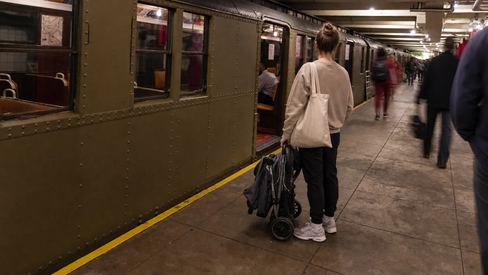 Caregiver with a stroller waiting on a New York City transit platform during a child care commute.