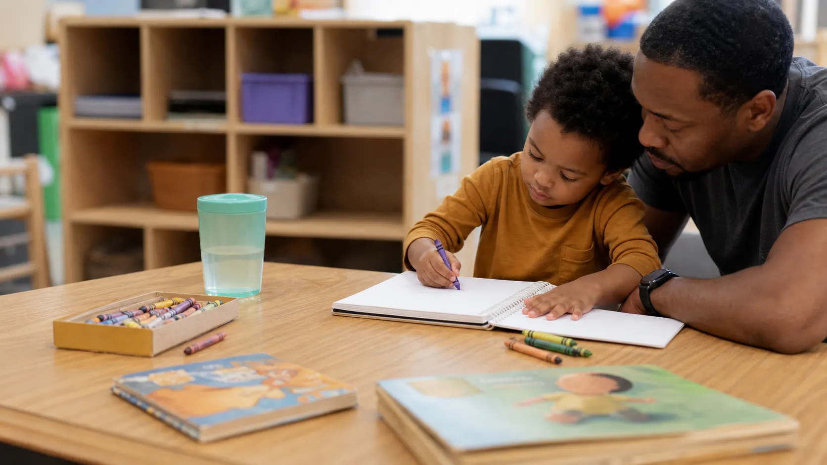 Table with preschool supplies, books, and a parent notebook in an early childhood classroom.