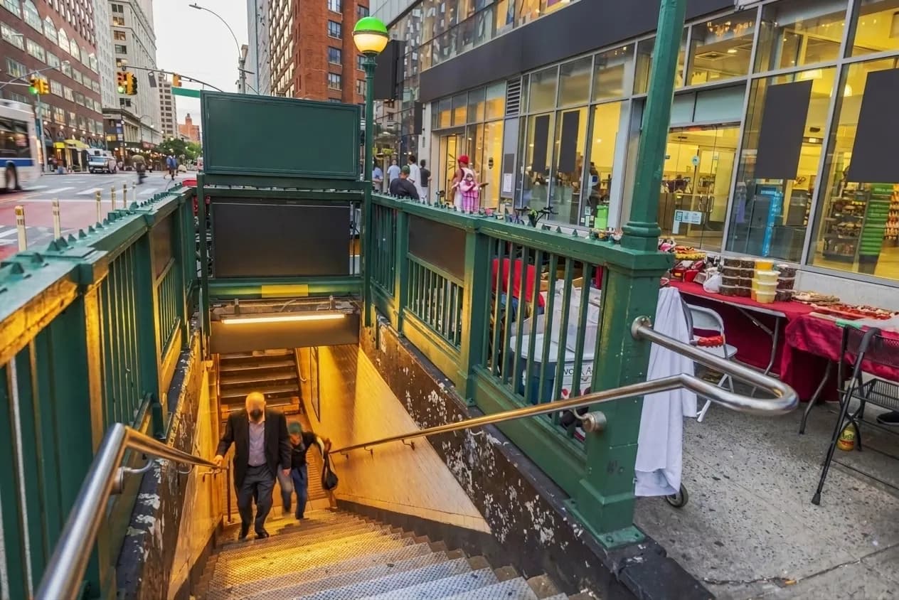 Green-railed subway entrance on a busy New York street at dusk