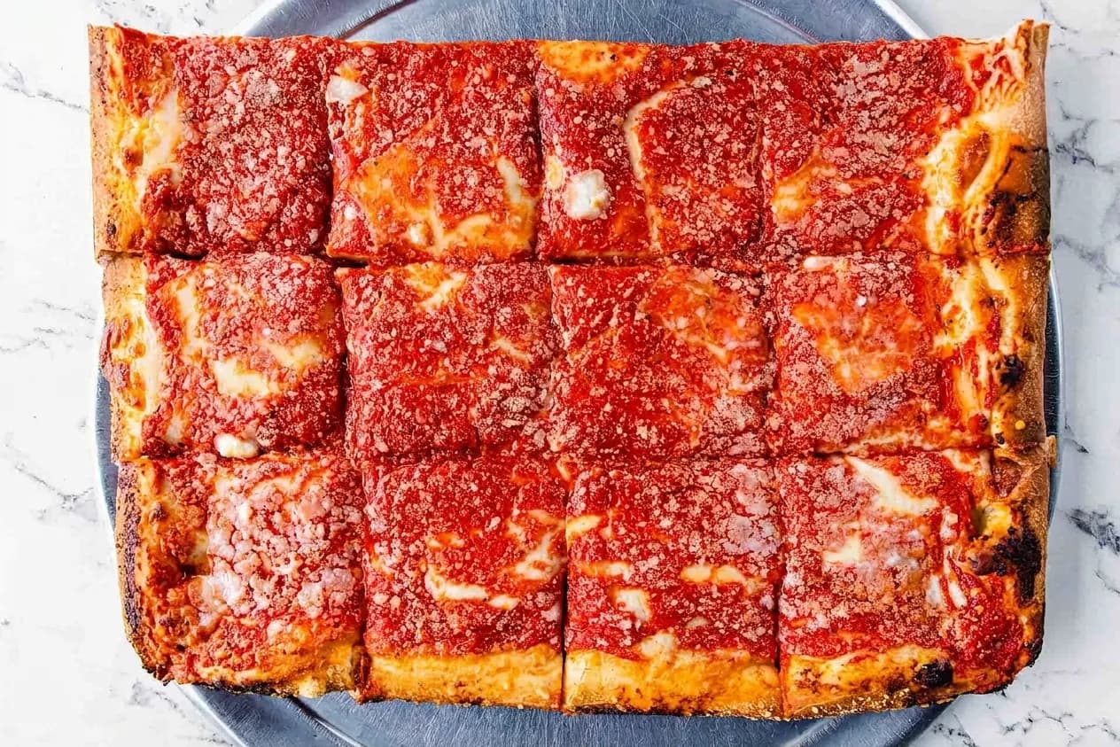 Overhead view of a Sicilian square pie cut into twelve pieces on a steel tray