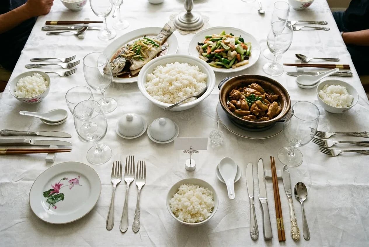 A shared table of dishes seen from above with rice bowls and chopsticks