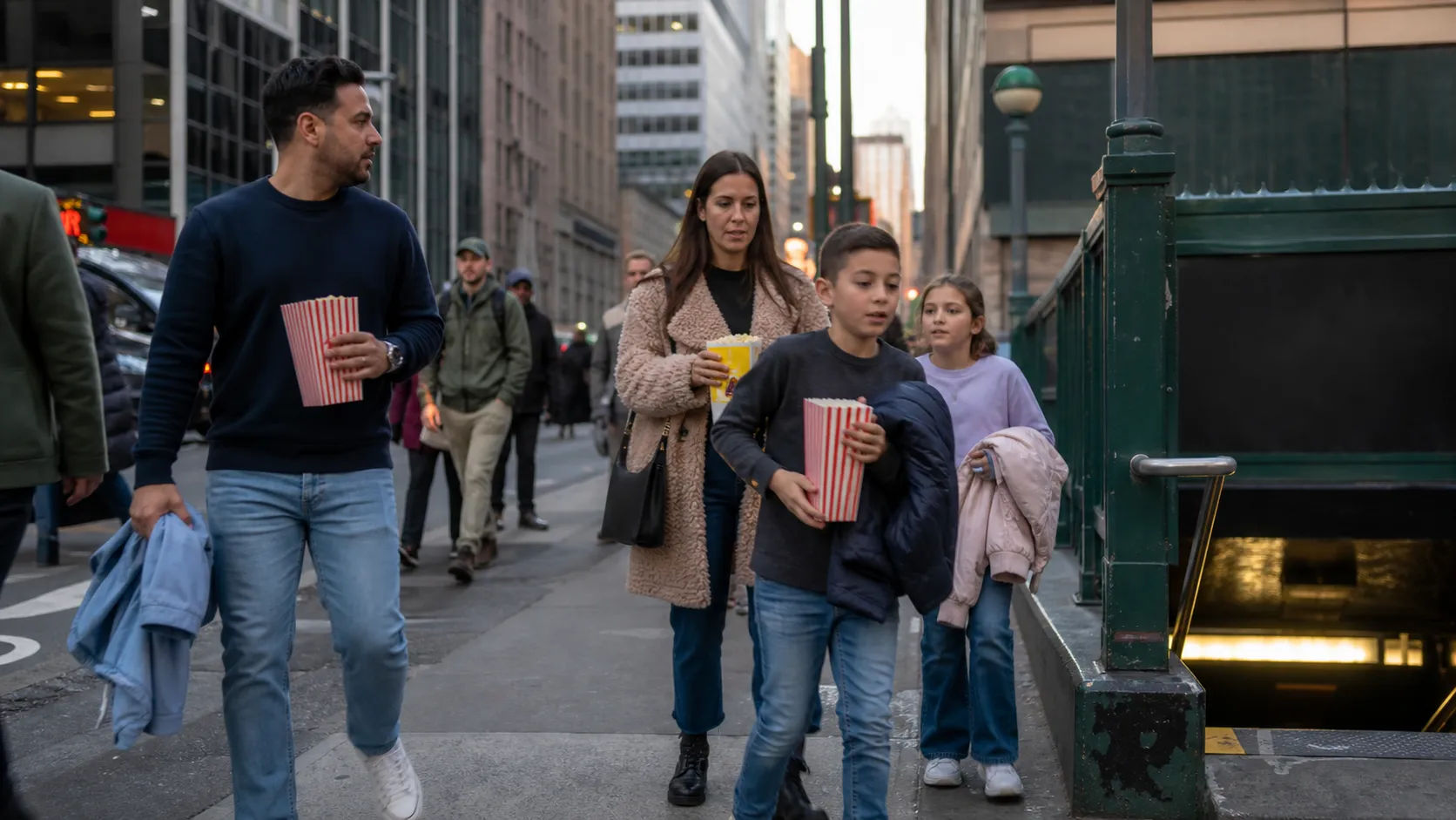 Families move through a busy Times Square sidewalk near a subway entrance before a movie outing.