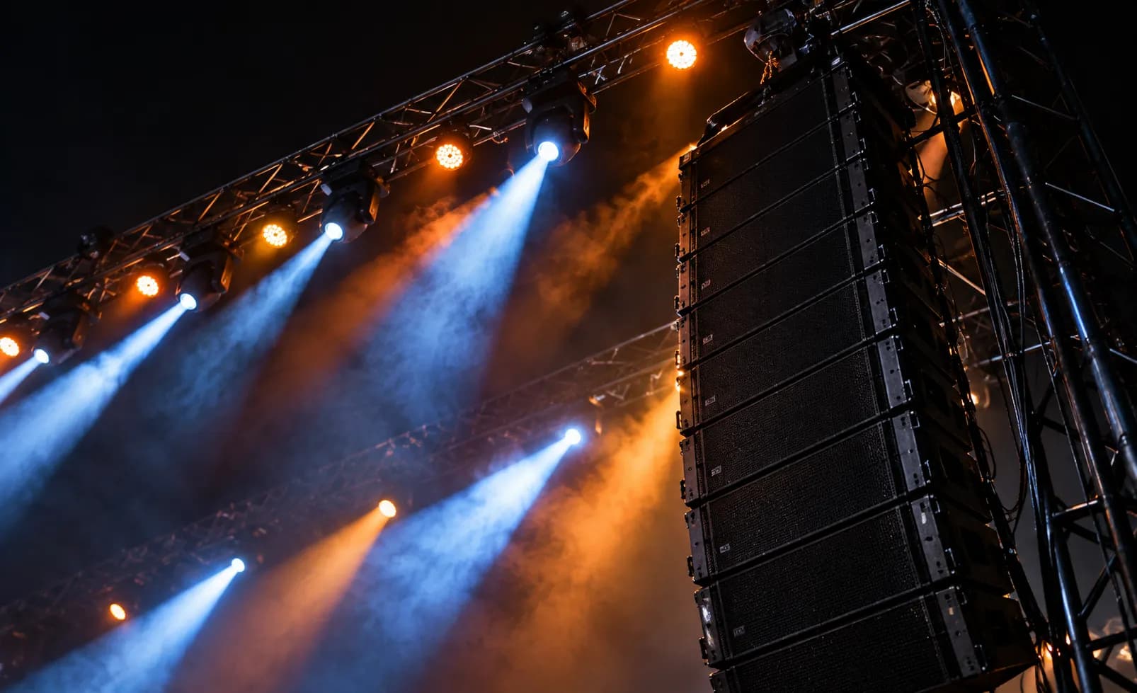 A large speaker stack and lighting rig seen from below against a dark sky