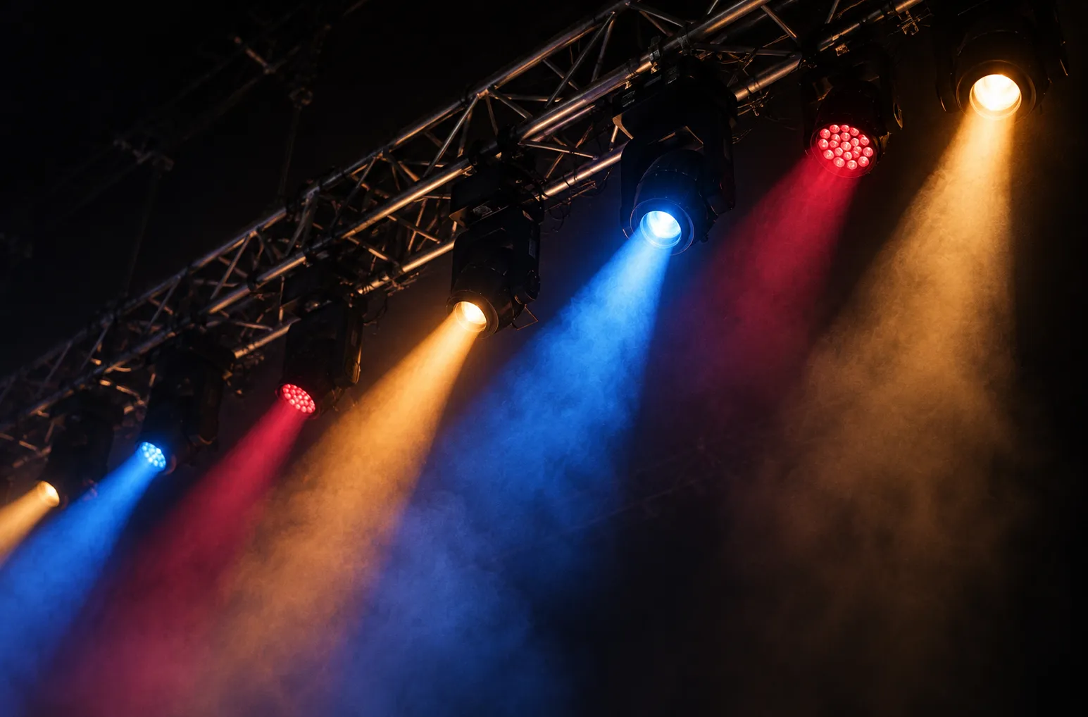 Stage lighting rigs hanging from a steel truss above an empty floor