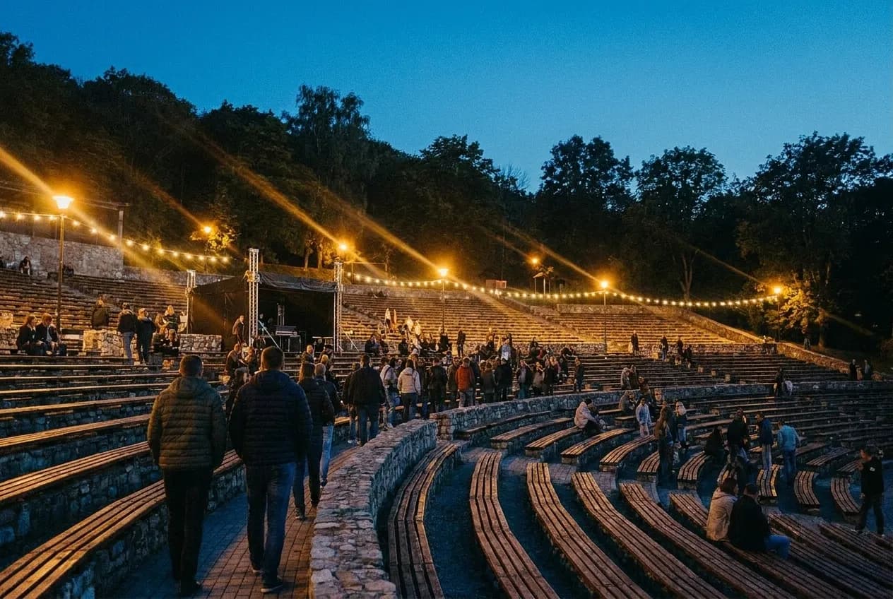 A broad terraced open-air venue filling with people before an evening event under warm lamps and a late blue sky