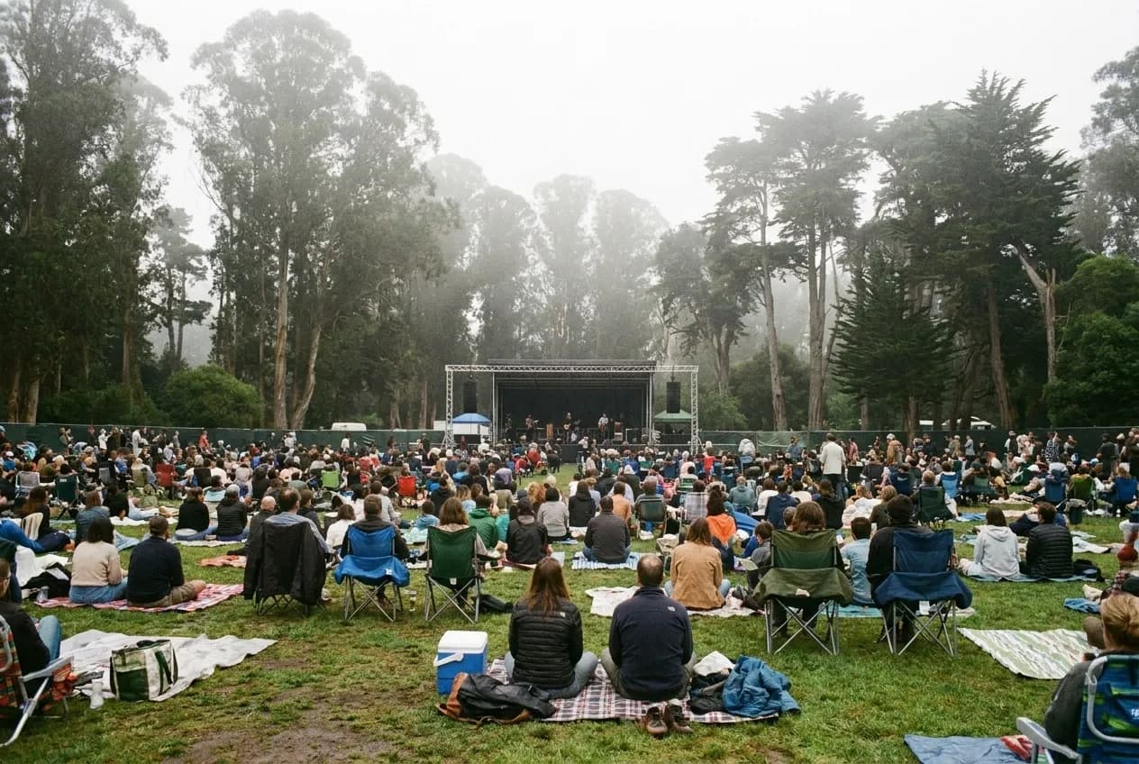 A crowd on blankets in a park in front of a small outdoor stage