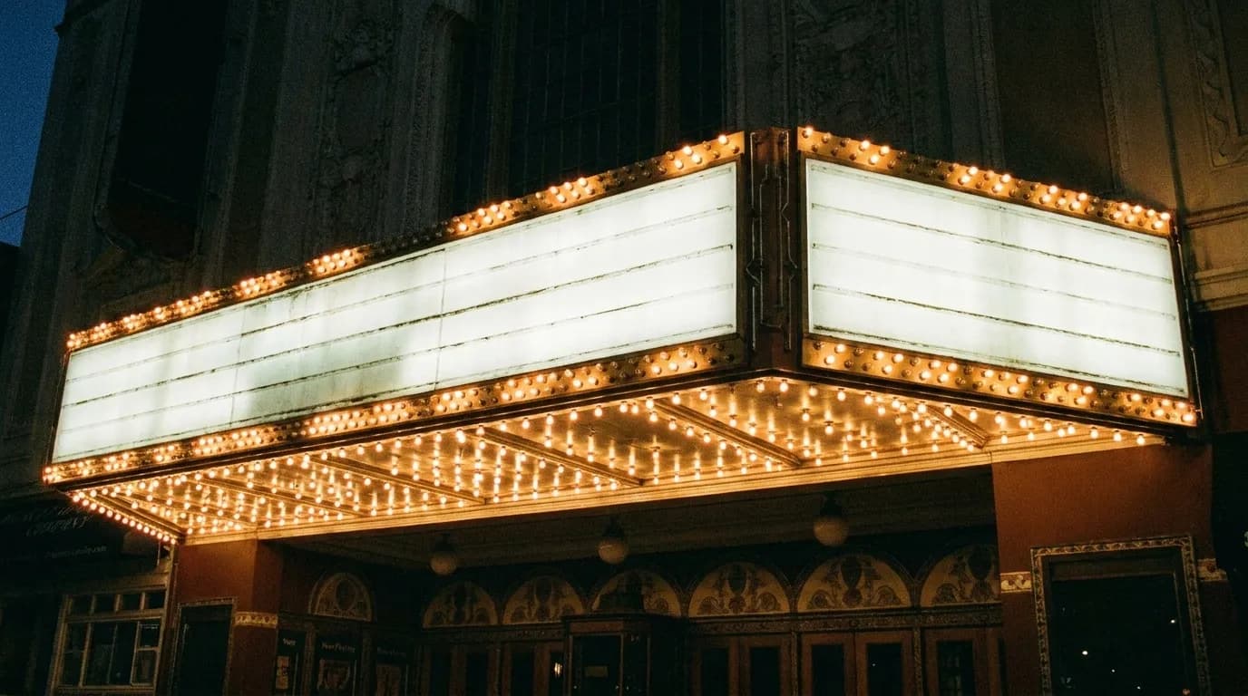 A theatre marquee lit with bare bulbs above a sidewalk on a dark city street