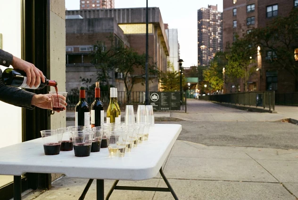 Wine table at Lower East Side gallery opening with plastic cups and bottles on folding table