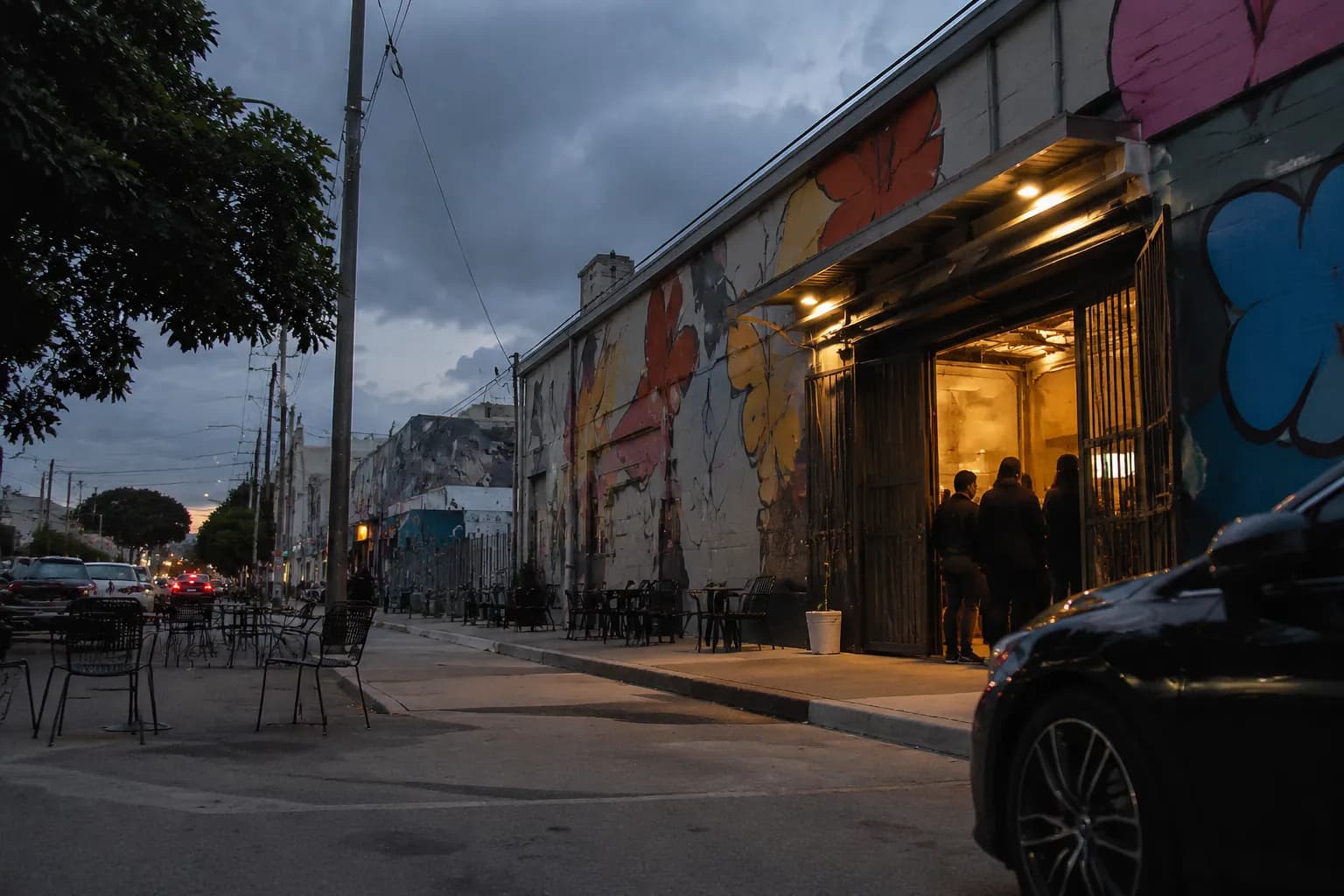 Wynwood street at dusk with warehouse venue doors open and colorful murals on building facades