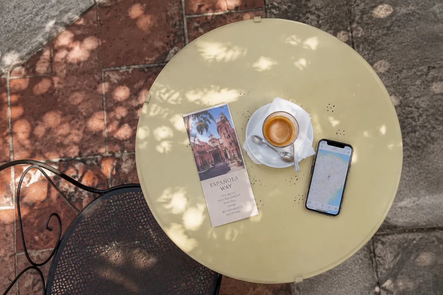 Overhead view of a café table on Española Way with venue flyer, coffee, and phone showing a map
