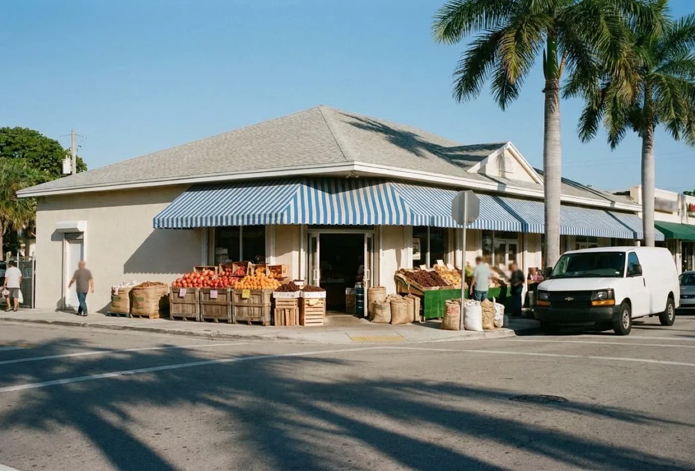 A low-rise corner market building in Miami with a striped awning, produce crates outside and delivery vans parked along a wide street