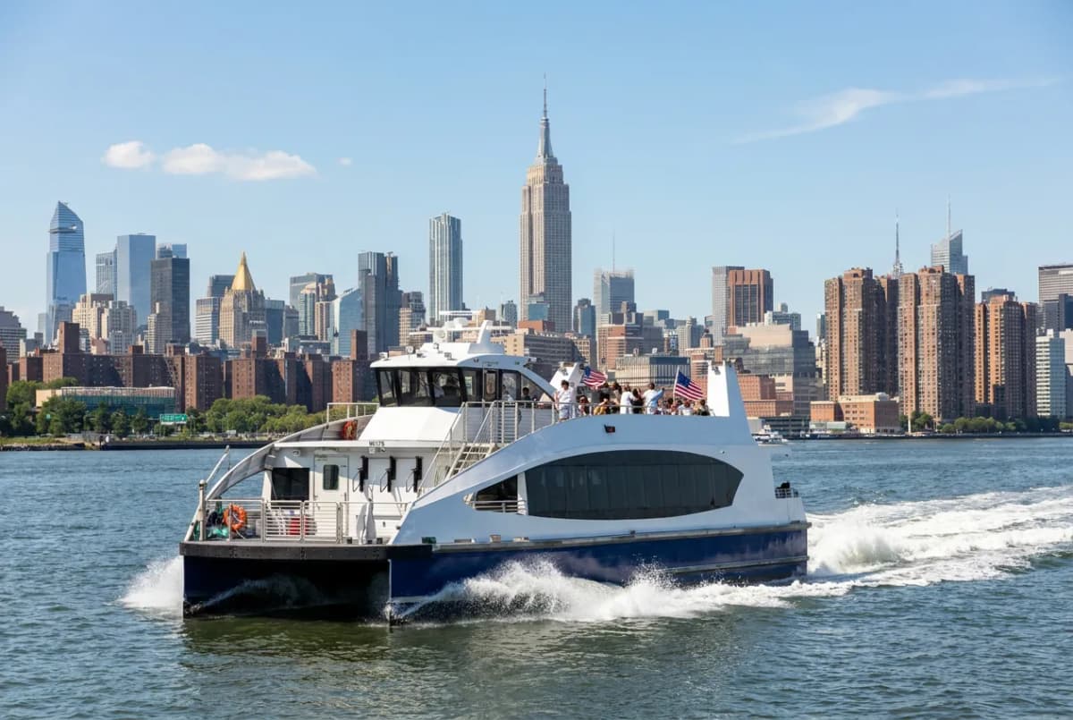 A modern passenger ferry cutting across New York Harbor on a bright summer day with the skyline behind it