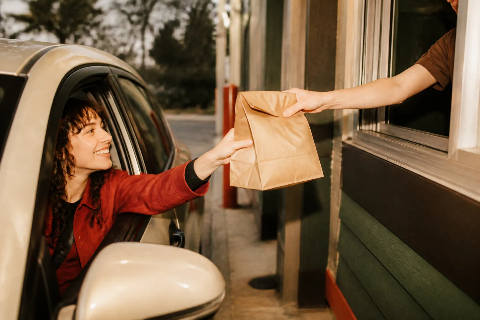 A hand reaching from a car to a drive-thru window receiving a food bag