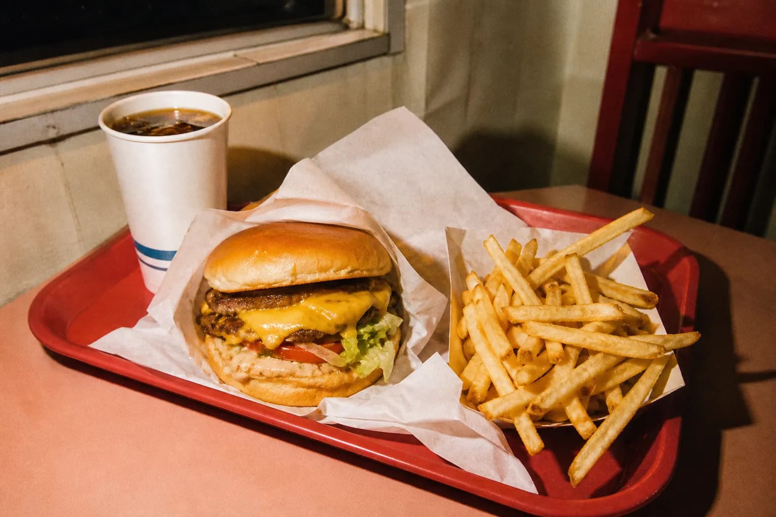 A fast food tray holding a burger and golden fries under warm overhead light