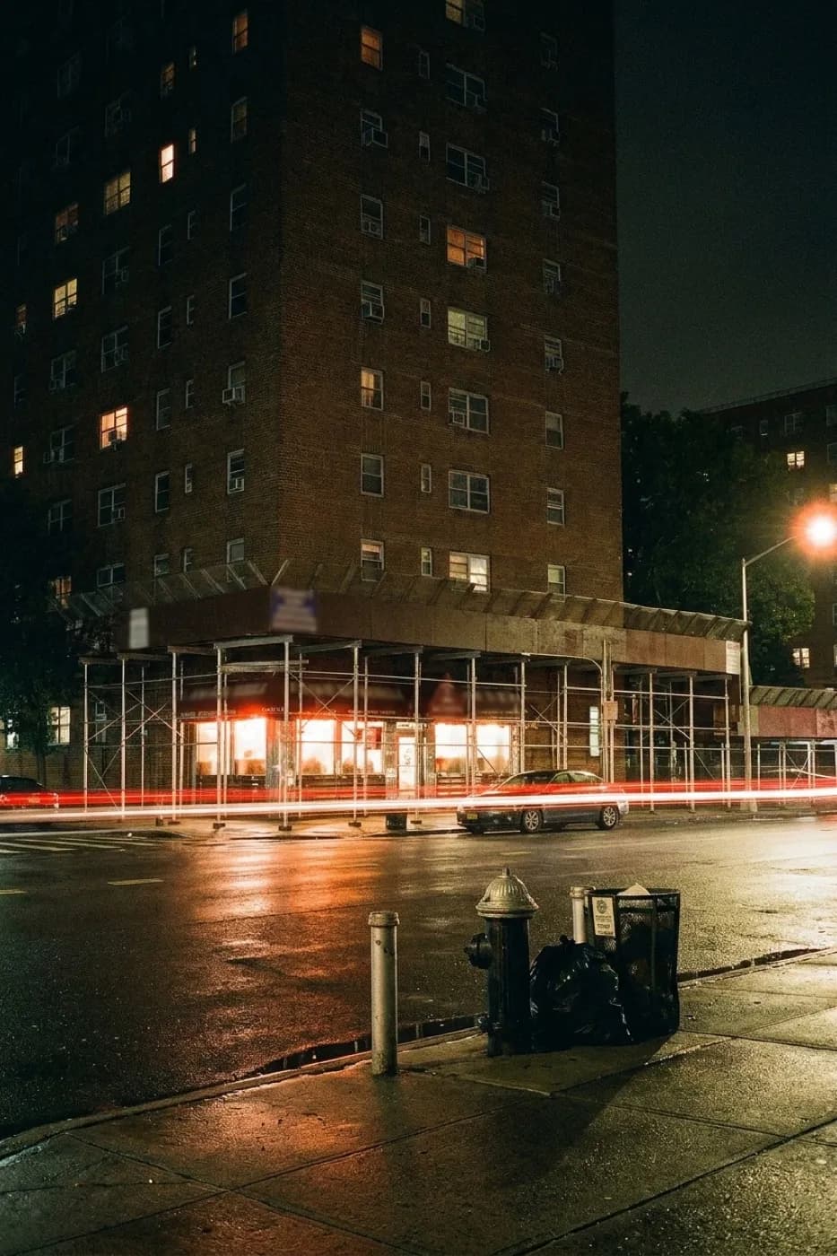 A lit corner diner in Brooklyn after midnight with steamed windows, an empty pavement outside and a single car passing under a streetlight