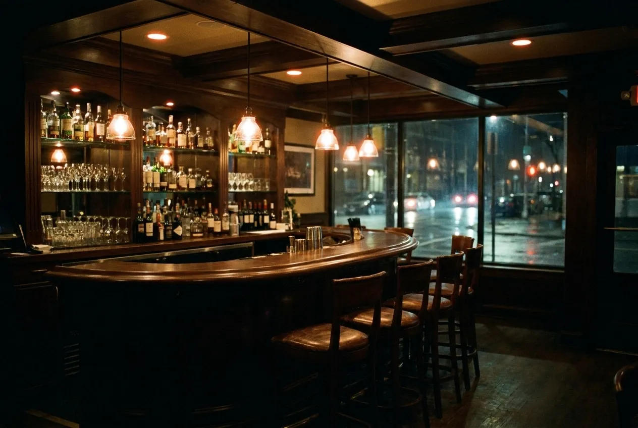 A late-night restaurant interior with a lit bar, empty stools and warm light spilling onto a dark street through the window