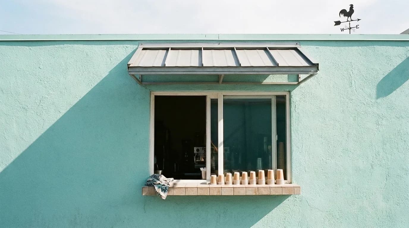 A walk-up coffee window in a pastel wall with a narrow ledge and shuttered awning above
