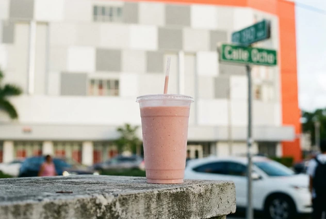 Mamey batido in plastic cup with straw on concrete ledge with Calle Ocho street sign behind