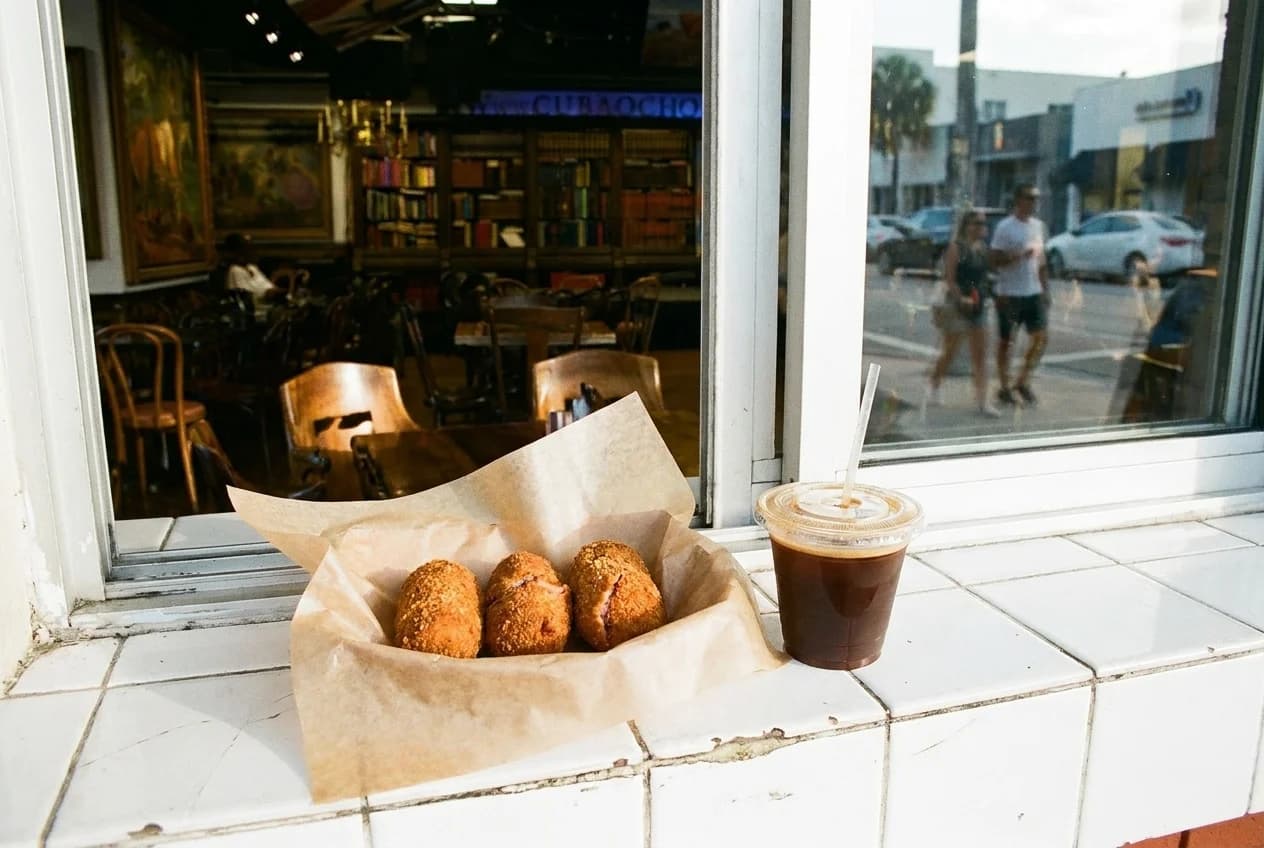 Three fried ham croquetas in waxed paper with a cortadito on a ventanita counter in Little Havana