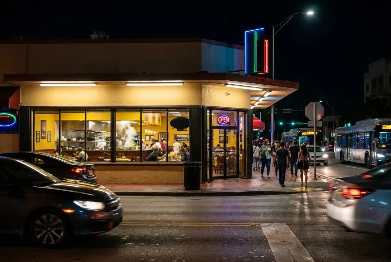 Night exterior of a brightly lit Cuban restaurant on Biscayne Boulevard in North Miami, with warm yellow light filling large windows and cars parked along the curb.