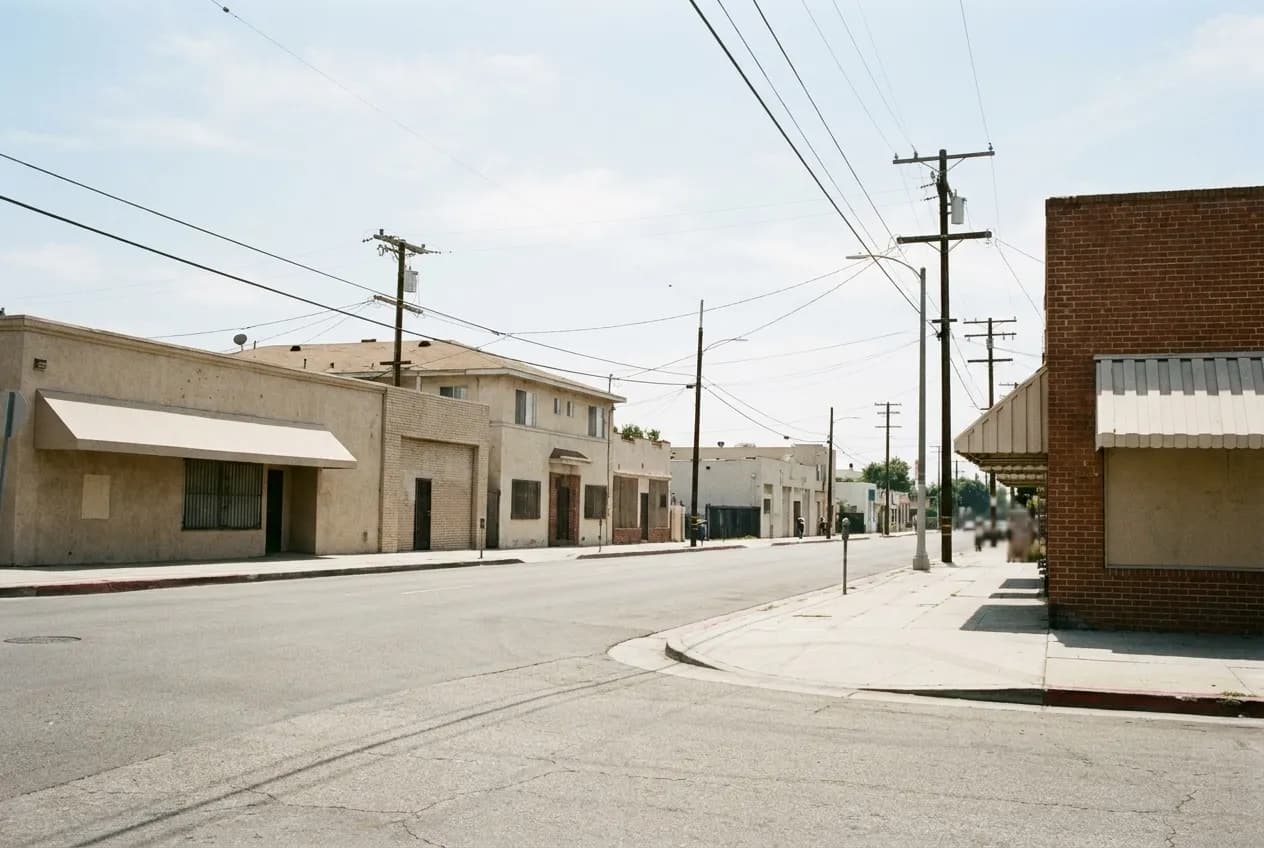 A quiet residential corner with low buildings and power lines under bright Los Angeles sky
