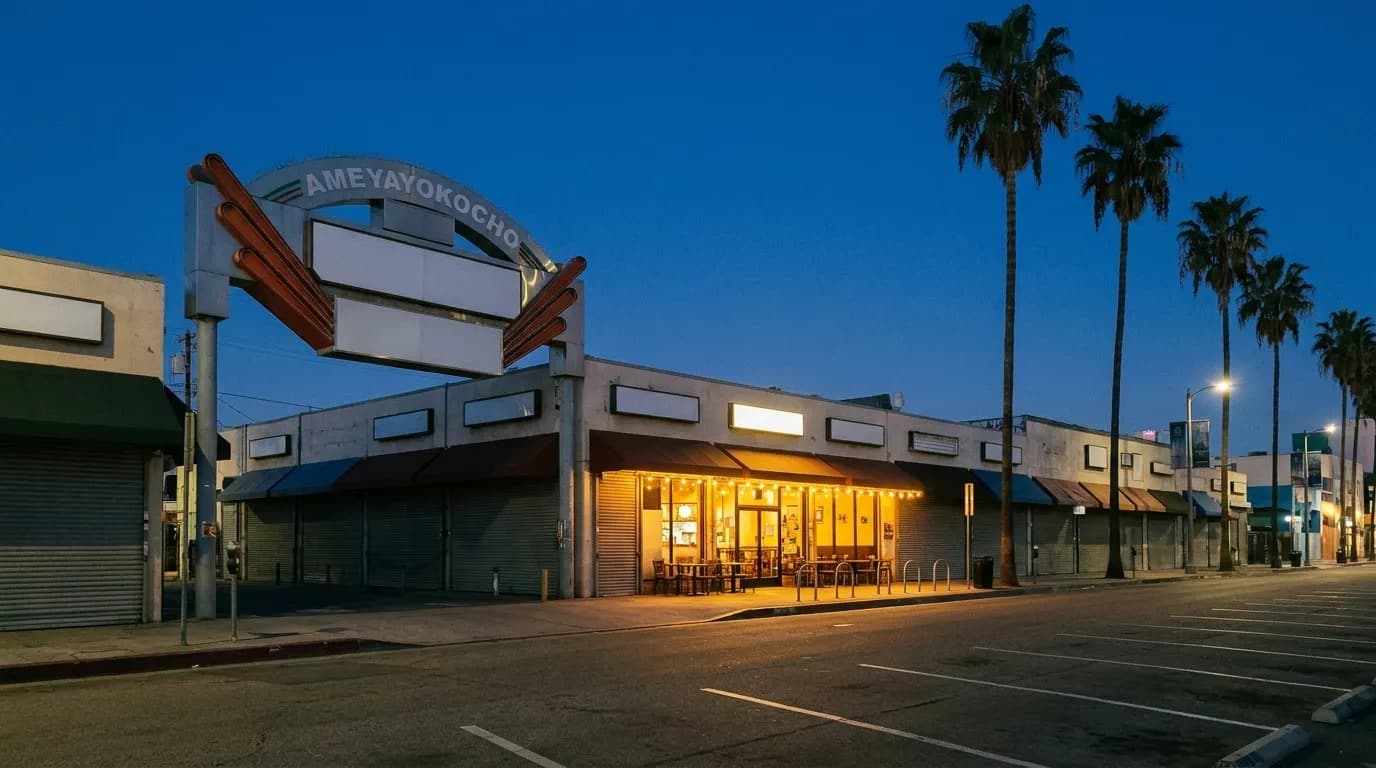 A quiet Los Angeles restaurant street on a Monday evening, most shopfronts dark with one lit dining room halfway down the block and empty parking spaces outside