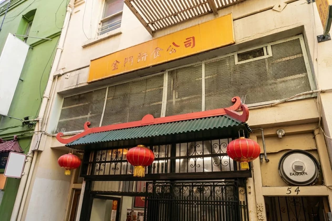 Warm fortune cookies stacked beside folded slips in a Chinatown factory setting