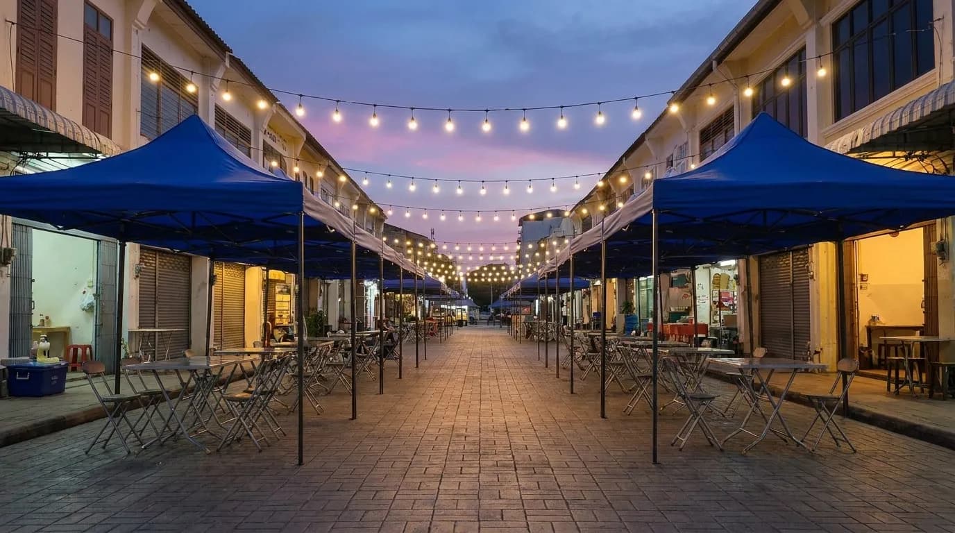 A closed-off city street set up for an evening festival with market canopies down both sides and strings of lights overhead, before the crowd arrives