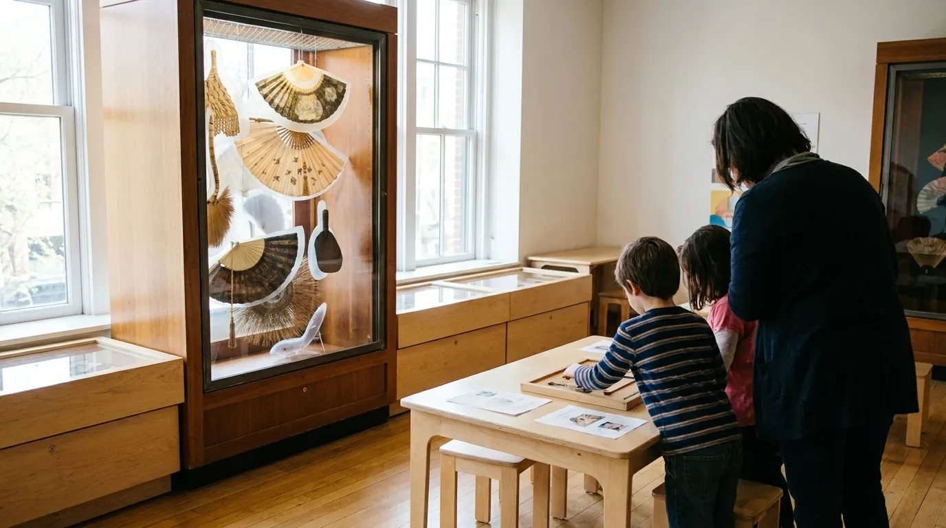 Children looking at a hands-on exhibit in a bright museum room with large windows, wooden tables and low display cases around them